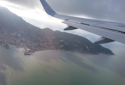 The wing of an airplane over the ocean and an island.