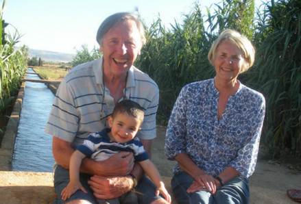 A man, woman, and child sitting on a low bridge by a field. Photo by Keith Moore.