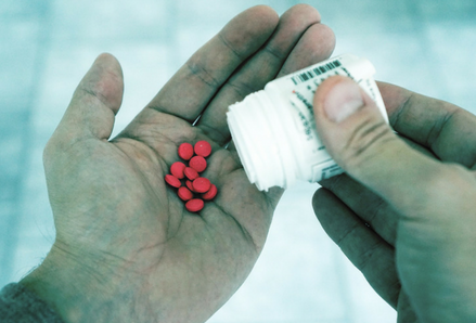 Two hands holding a pill bottle and red pills. Photo by TheDigitalWay, Pixabay.