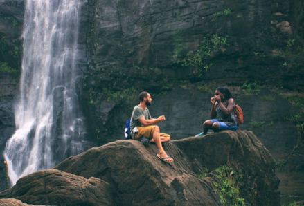 Two people sitting on a rock next to a waterfall. Photo by Nandhu Kumar, Pexels.