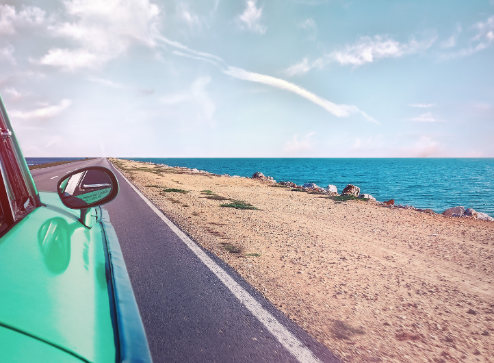 Green car driving down a coastal road